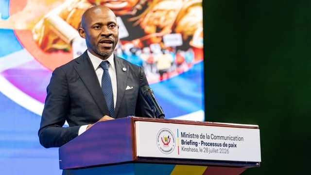 Patrick Muyaya, ministre de la Communication et porte-parole du gouvernement congolais, s'exprime au micro derrière un pupitre portant la mention « Ministère de la Communication, Briefing - Processus de paix, Kinshasa, le 28 juillet 2026 ».