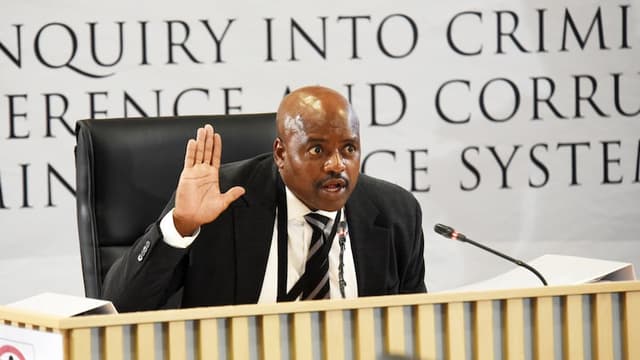 Un témoin en costume dépose à la barre devant la commission Madlanga, dans l'auditorium du Brigitte Mabandla Justice College à Pretoria.