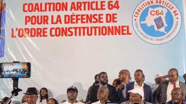 Les responsables de la Coalition Article 64 assis derrière une table drapée du drapeau congolais, devant une grande banderole blanche portant en lettres rouges « Coalition Article 64 pour la défense de l'ordre constitutionnel » et le logo C64 ; au premier plan, des caméras et des téléphones filment la séance.