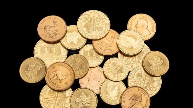 Une vingtaine de pièces d'or d'investissement (Krugerrand, Maple Leaf canadienne, Wiener Philharmoniker) posées en tas sur un fond noir