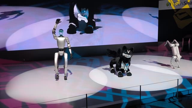 Un robot humanoïde Unitree G1 et un robot-chien Unitree Go2 présentés sur une scène d'exposition, sous les projecteurs.