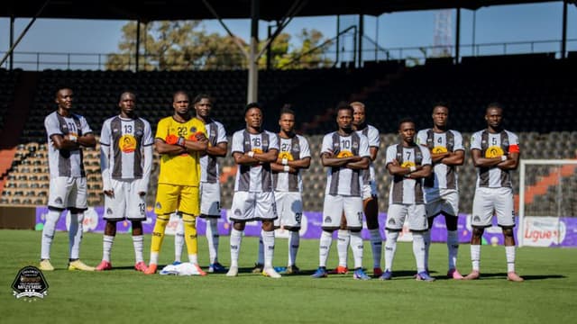 Le onze de départ du TP Mazembe, en maillot rayé noir et blanc, posant bras croisés sur la pelouse de leur stade à Lubumbashi avant un match.
