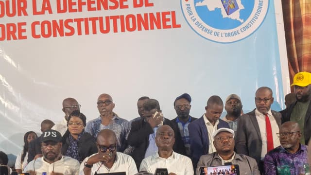 Les responsables de la Coalition Article 64 assis en conférence de presse derrière une table drapée du drapeau de la RDC, l'un d'eux lisant une déclaration au micro, sous une grande banderole blanche « pour la défense de l'ordre constitutionnel » et le logo C64 ; des caméras et téléphones filment la scène au premier plan.