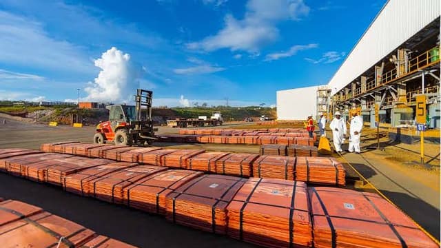 Piles de cathodes de cuivre alignées sur l'aire d'expédition de la mine de Tenke Fungurume, avec un chariot élévateur et des ouvriers en combinaison blanche