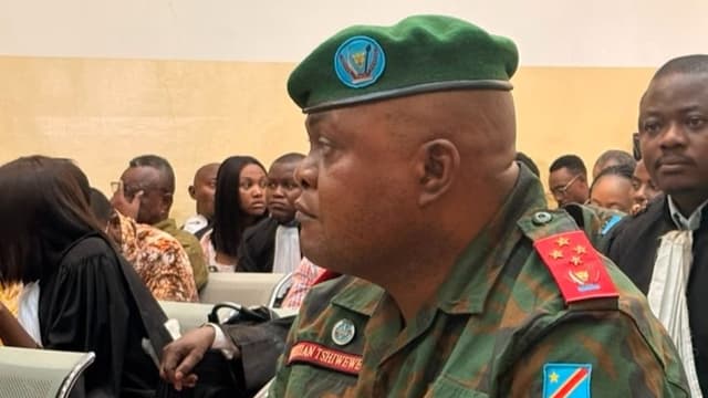 Le général d'armée Christian Tshiwewe, en tenue de camouflage des FARDC et béret vert orné des armoiries de la RDC, insigne de général quatre étoiles et plaque « Christian Tshiwewe » sur la poitrine, assis dans la salle d'audience de la Haute Cour militaire à Kinshasa.