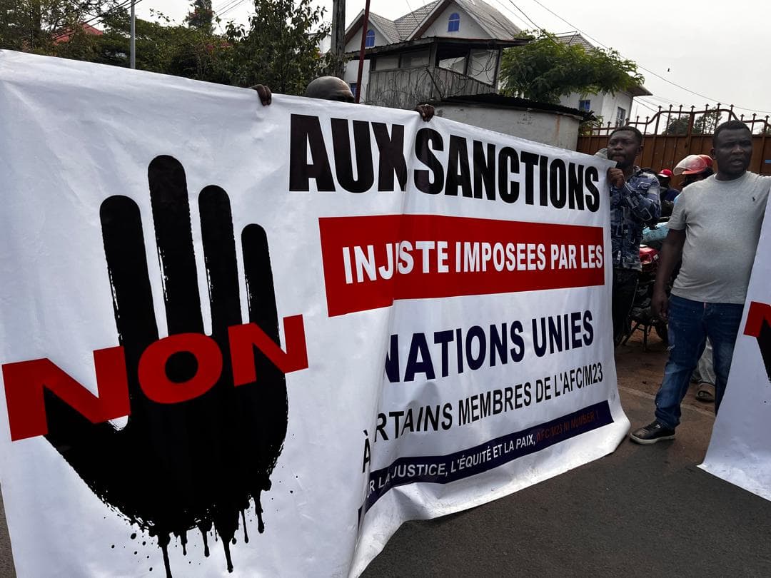 Des manifestants déploient dans une rue de Goma une grande banderole portant un symbole de main et le mot « NON » en rouge, avec l'inscription « Aux sanctions injustes imposées par les Nations unies à certains membres de l'AFC/M23 ».