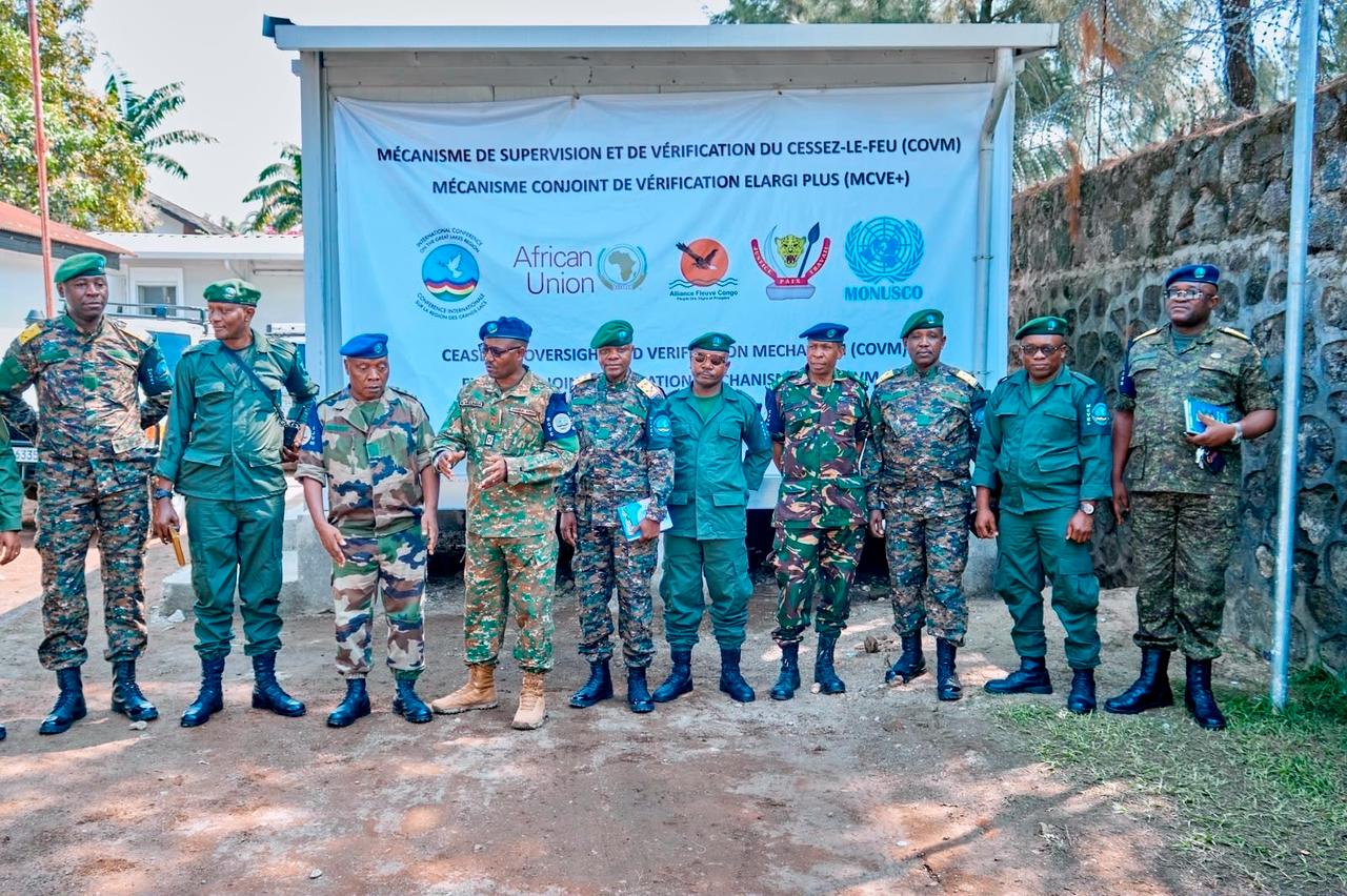 Une quinzaine d'officiers en tenues militaires différentes, dont plusieurs portant le béret bleu de l'ONU et des bérets verts, alignés devant une banderole blanche portant l'inscription « Mécanisme de supervision et de vérification du cessez-le-feu (COVM) ,  Mécanisme conjoint de vérification élargi plus (MCVE+) » et les logos de la CIRGL, de l'Union africaine, de l'Alliance Fleuve Congo, des FARDC et de la MONUSCO, dans une cour en terre battue à Goma.