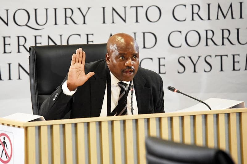 Un témoin en costume dépose à la barre devant la commission Madlanga, dans l'auditorium du Brigitte Mabandla Justice College à Pretoria.