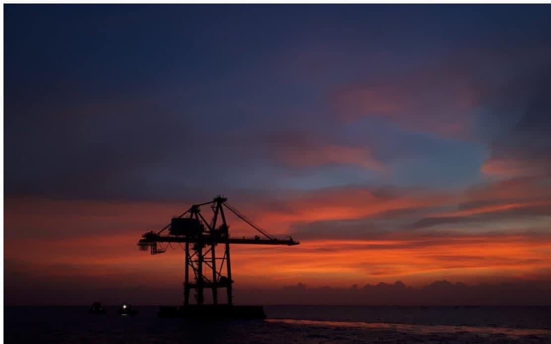 Silhouette d'une installation pétrolière offshore dressée en pleine mer, se découpant sur un ciel embrasé au coucher du soleil