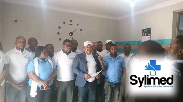 Des responsables du Syndicat libre des médecins (SYLIMED), en polos bleus, entourent un porte-parole lisant une déclaration au micro lors d'un point de presse à Kinshasa