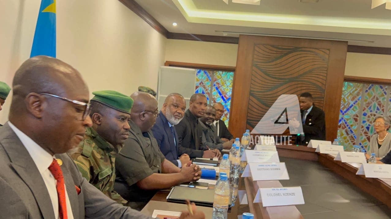 Des responsables civils et des officiers en tenue de camouflage de l'AFC/M23 assis en rang le long d'une table de réunion, face à une délégation, dans une salle de conférence à Goma