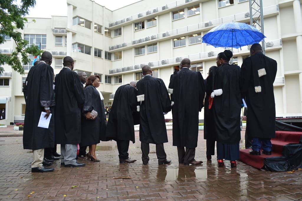 Un groupe de magistrats congolais en robe noire, réunis dans la cour intérieure du nouveau Palais de justice de la commune de la Gombe, à Kinshasa, devant un bâtiment moderne de plusieurs étages.