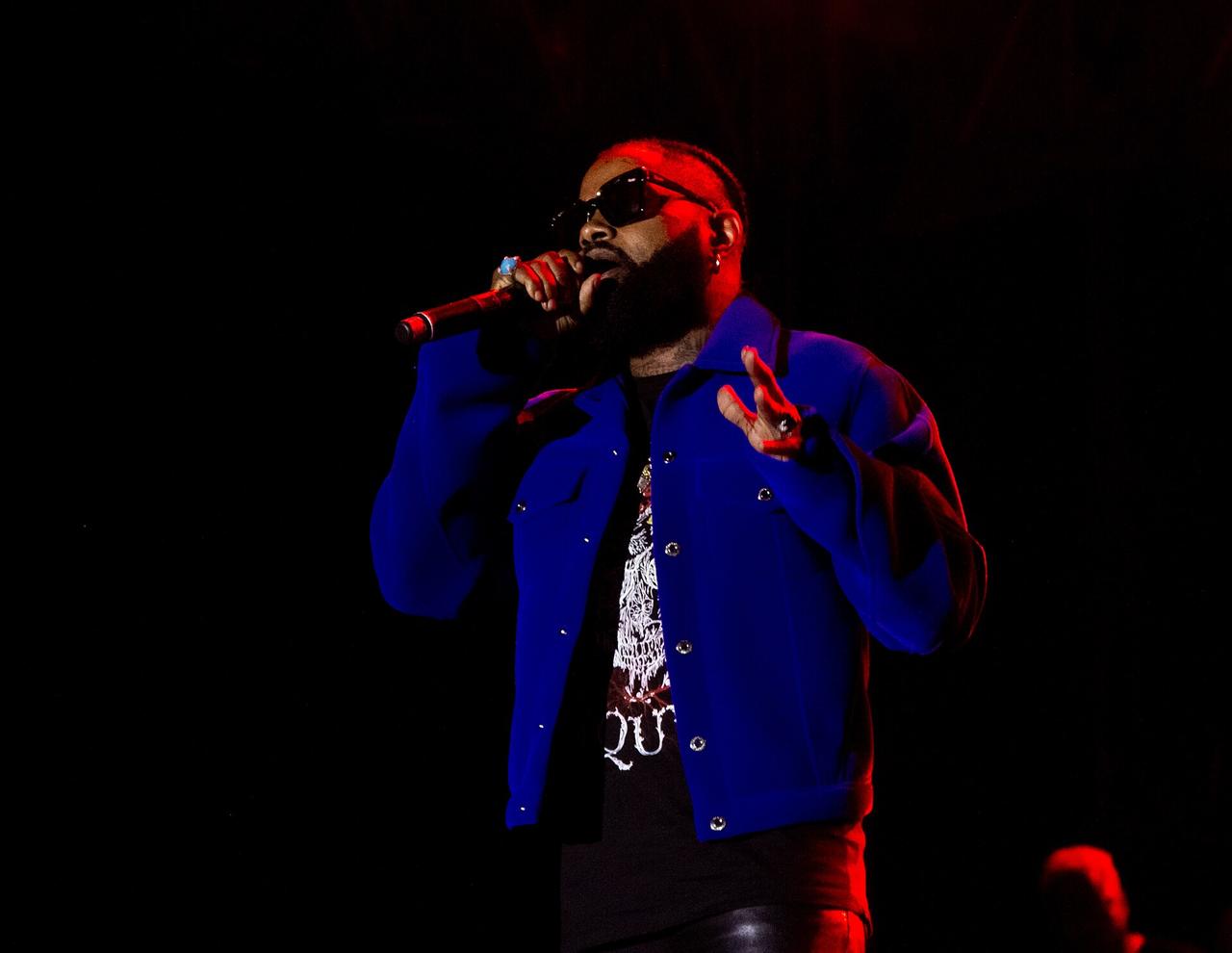 Le chanteur congolais Ferré Gola, veste bleue et lunettes de soleil, chante au micro sous des projecteurs rouges sur une scène de concert.