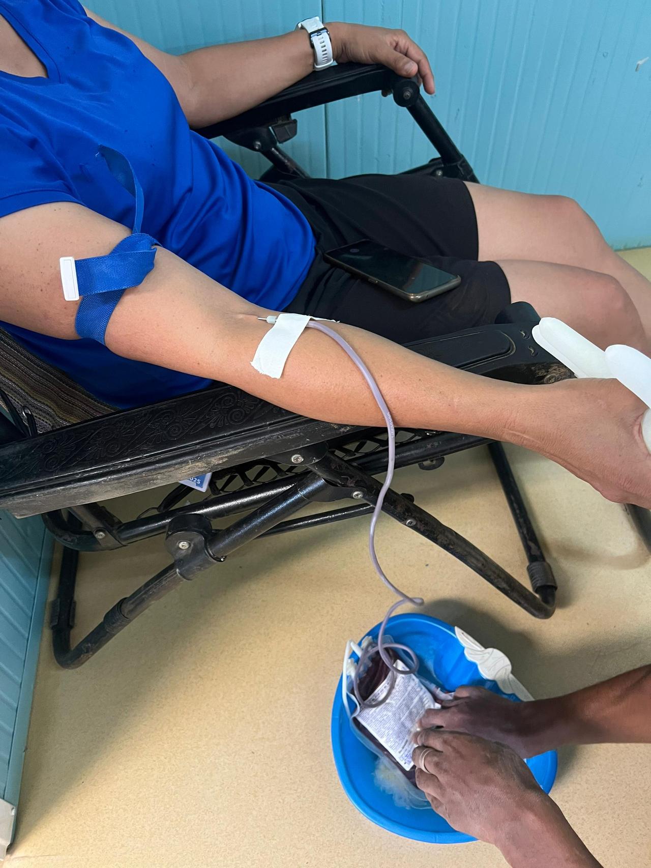 Une donneuse allongée sur un lit de prélèvement, le bras garrotté et perfusé, tandis qu'un agent de santé maintient la poche de sang posée dans une bassine bleue au sol, au Centre de transfusion sanguine de Beni.