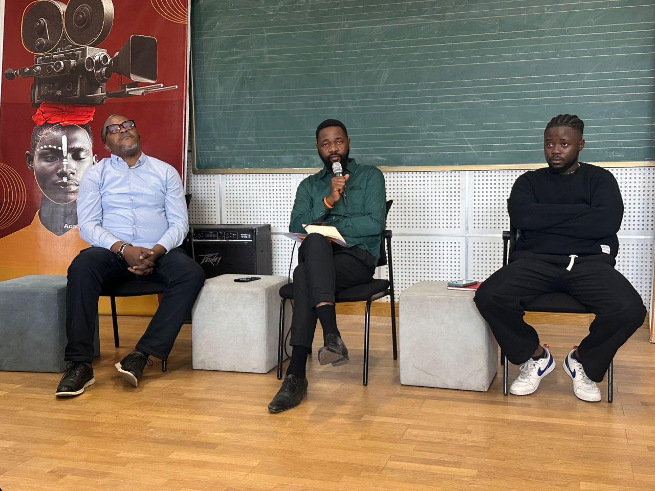 Trois organisateurs du FICKIN assis devant une affiche du festival lors de la conférence de presse de la 13e édition à Kinshasa, l'un d'eux parlant au micro