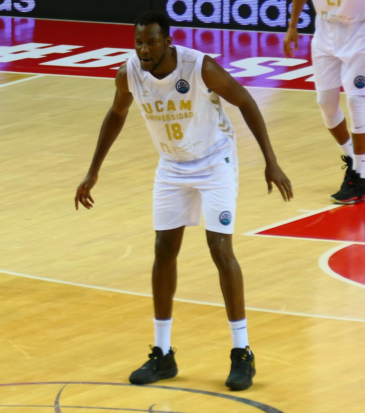 Le basketteur congolais Jordan Sakho, en maillot blanc floqué du numéro 18, bras écartés en position défensive sur un parquet, pendant un match de championnat.