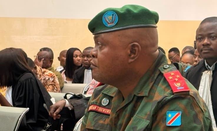 Le général d'armée Christian Tshiwewe, en tenue de camouflage des FARDC et béret vert orné des armoiries de la RDC, insigne de général quatre étoiles et plaque « Christian Tshiwewe » sur la poitrine, assis dans la salle d'audience de la Haute Cour militaire à Kinshasa.
